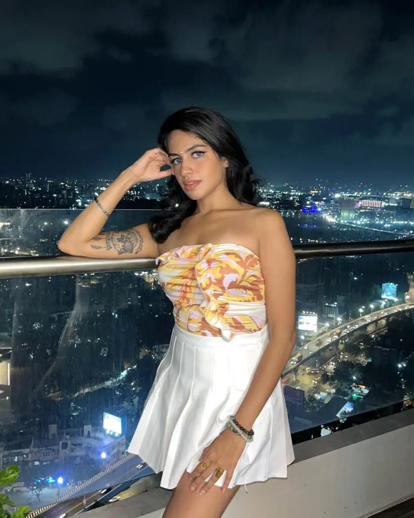 Image of Sharkshe aka Shakshi Shetty wearing a white dress with a tattoo on her arm.