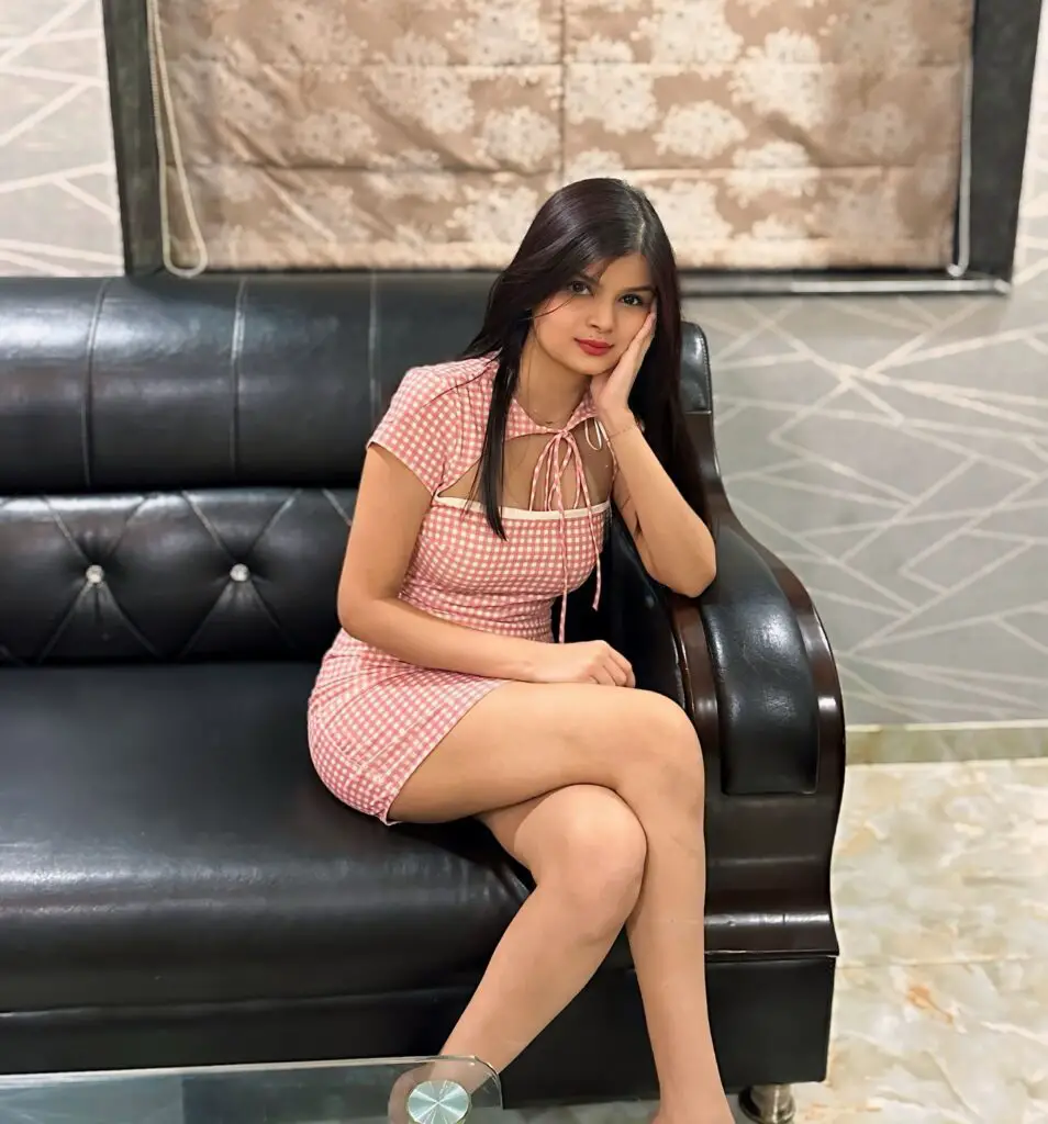 in a pink dress sitting on a black couch. Krutika Ojha, the YouTube streamer, looking stylish and relaxed.